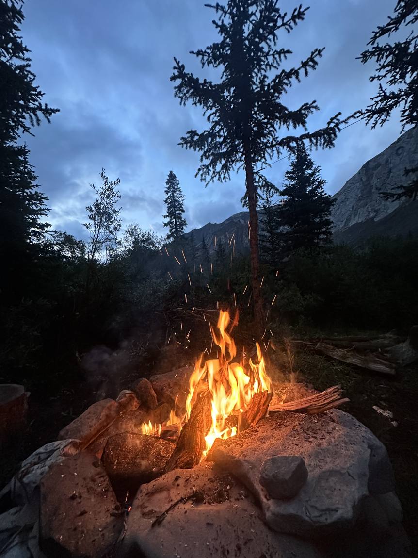 Camp fire under the Alberta mountains at dusk
